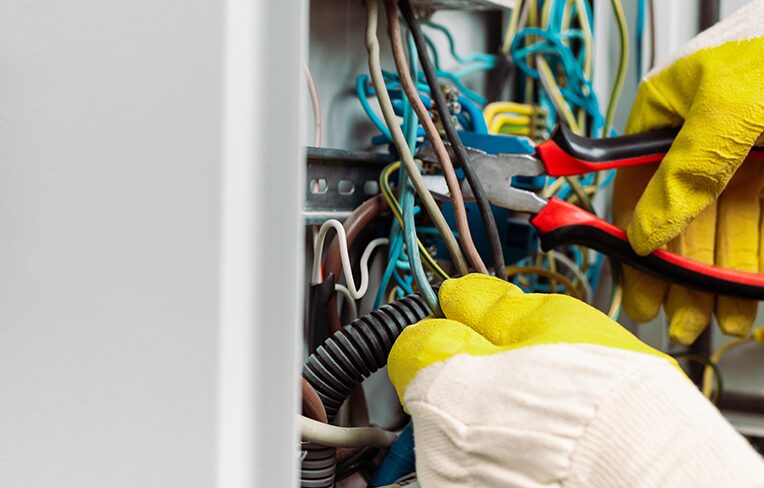 atelec bordeaux électricien ajuste des fils multicolores sur panneau électrique avec pince coupante et gants de sécurité