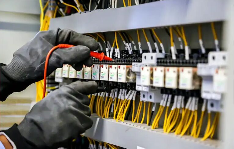 Électricien atelec à Bordeaux vérifiant un tableau électrique, fils jaunes et tournevis sous gants de protection