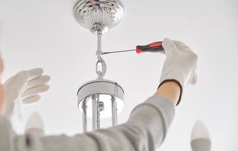 Electricien atelec bordeaux installant un lustre chromé moderne au plafond avec un tournevis